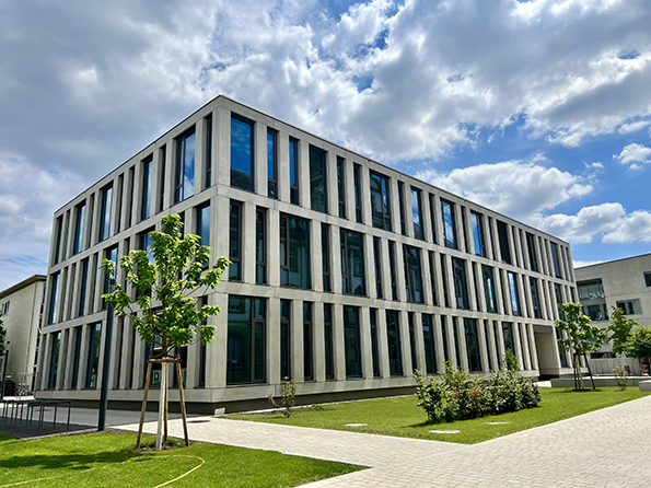 Modernes, mehrst&ouml;ckiges B&uuml;rogeb&auml;ude mit Betonfassade und gro&szlig;en Fensterfronten unter blauem Himmel.